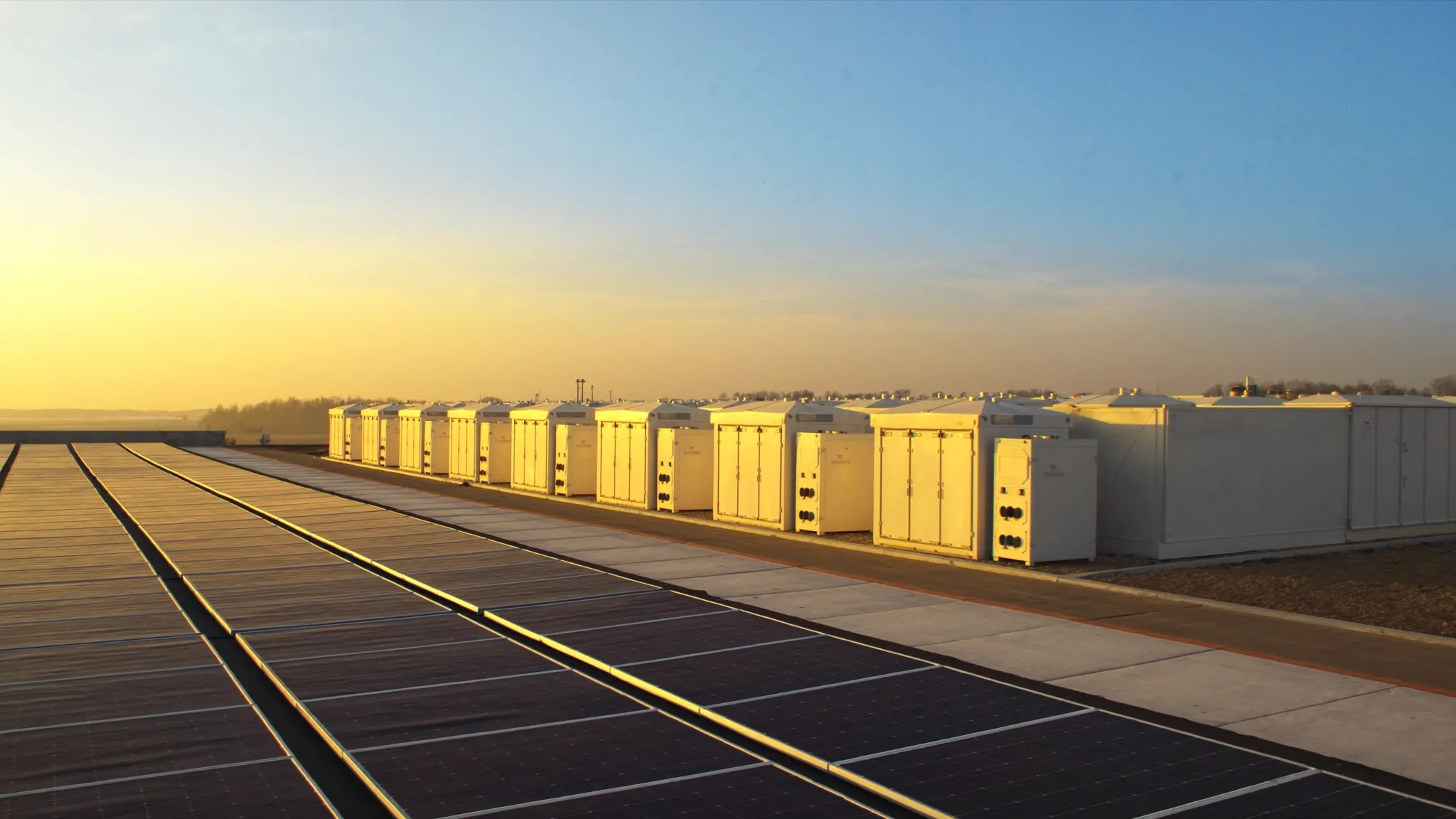 Commercial battery storage cabinets beside a rooftop solar array at a northern Illinois industrial facility at golden hour, representing the ComEd DG Rebate that pays $250 per kW of solar and $250 per kWh of storage