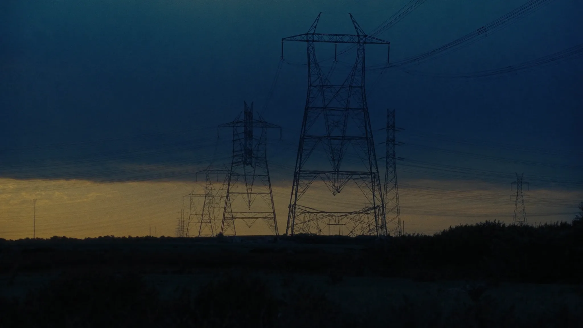 High-voltage transmission towers and power lines across an Illinois prairie at dusk, representing rising commercial electricity and grid capacity costs
