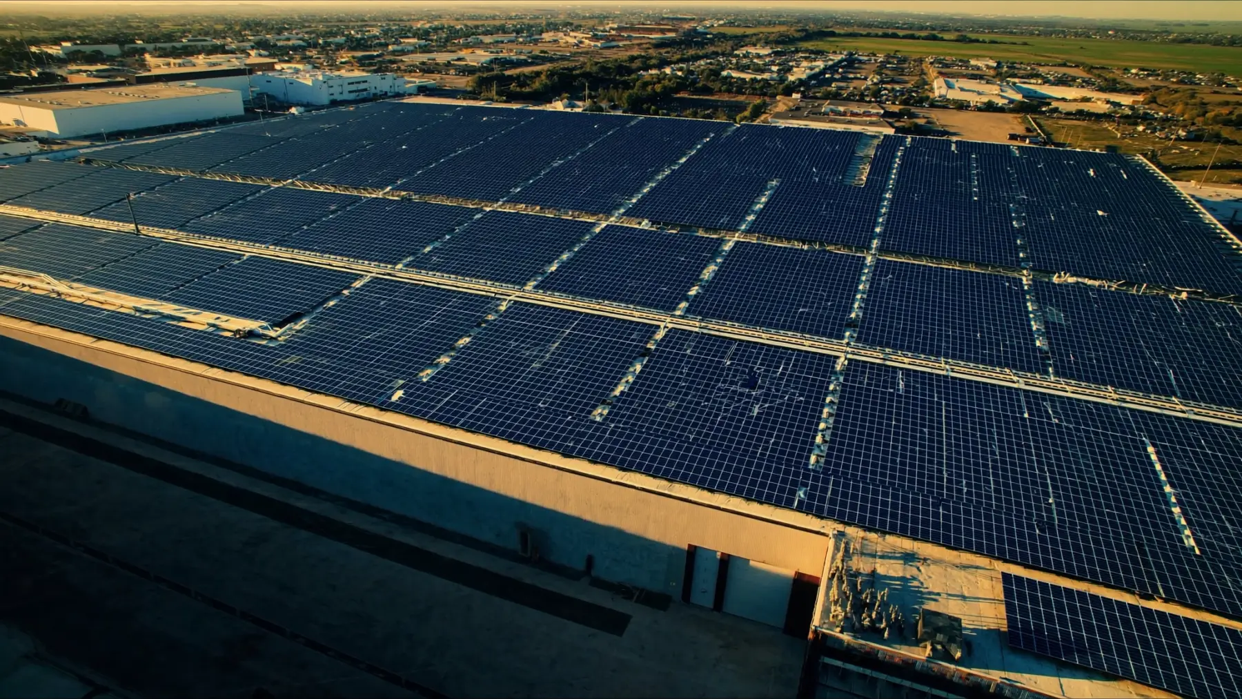 Aerial view of an expansive commercial rooftop solar array on a large industrial building at golden hour, representing the 30% commercial solar ITC and the July 4, 2026 begin-construction safe-harbor deadline